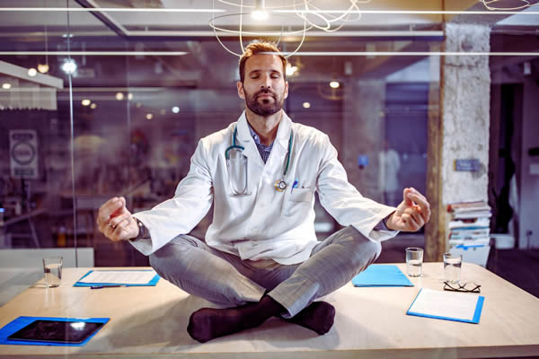 Ein Heilpraktiker sitzt meditierend auf seinem Schreibtisch